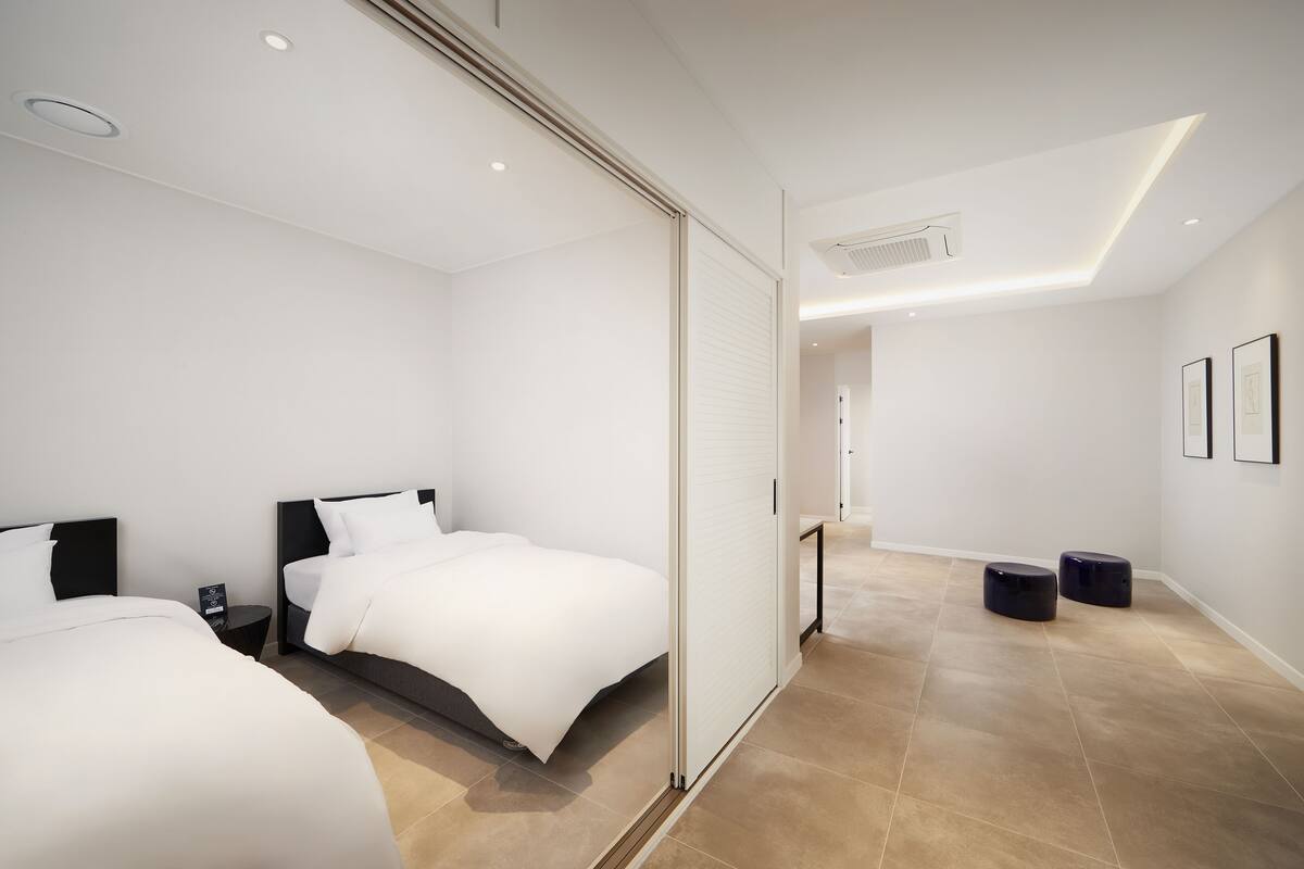 A modern hotel room with two beds, a sliding door, and a small table.