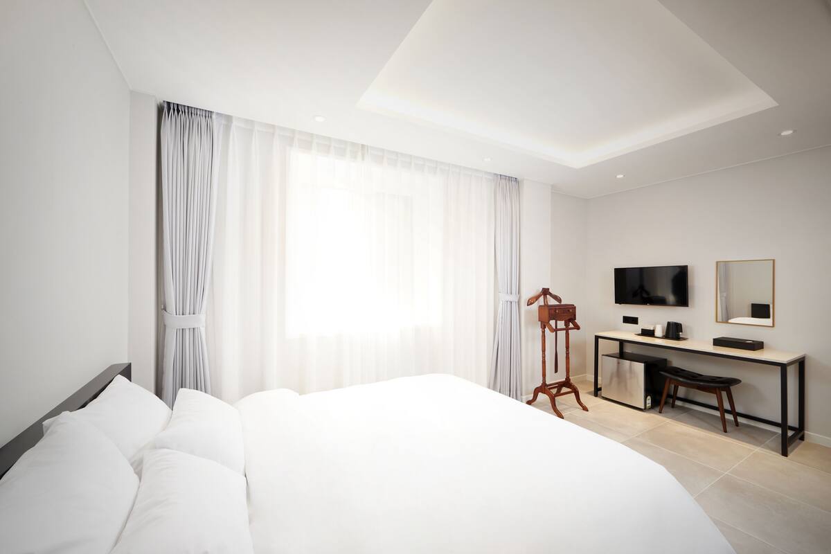 A modern hotel room with a large bed, a desk, a television, and a mirror.