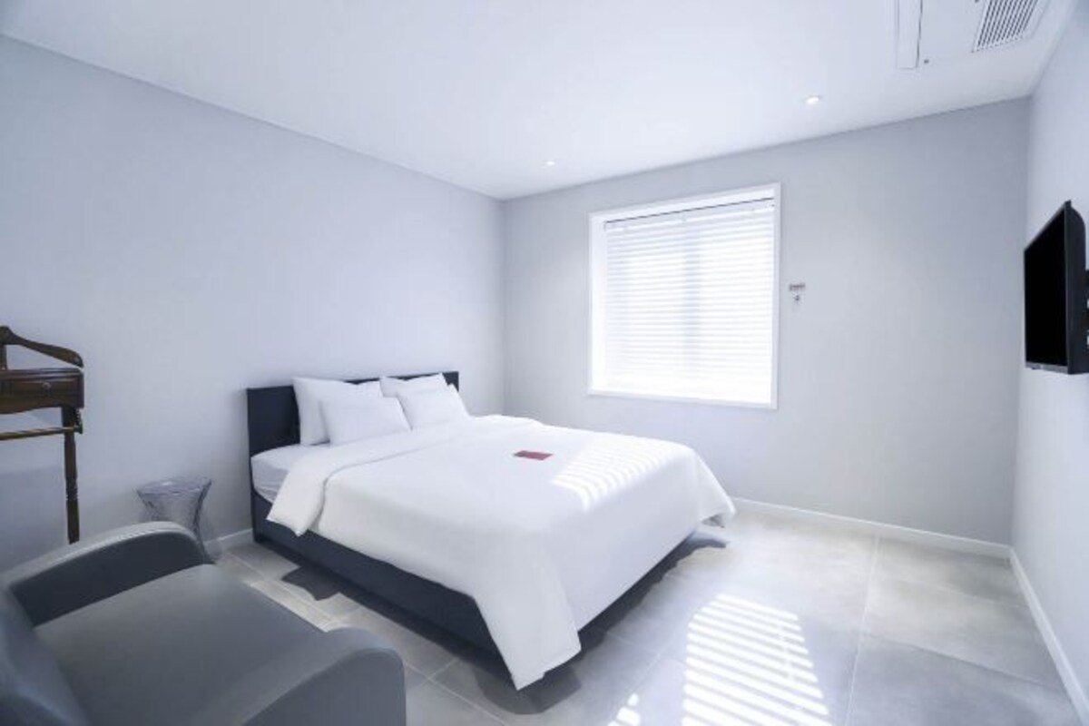 Ein modernes Schlafzimmer mit einem Bett, einem Sessel und einem Fernseher an der Wand.