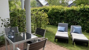 An outdoor patio with a glass table, two chairs, and two lounge chairs with cushions. - Exclusive apartment with private sauna, high-quality kitchen (Zingst)