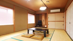 Une pièce de style japonais traditionnel, avec un sol recouvert de tatamis, une table basse, des portes coulissantes et un téléviseur.