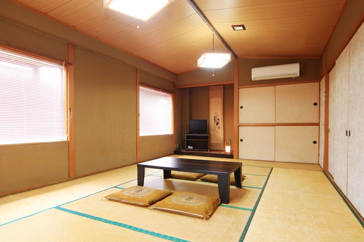 A traditional Japanese room with tatami flooring, a low table, sliding doors, and a television.