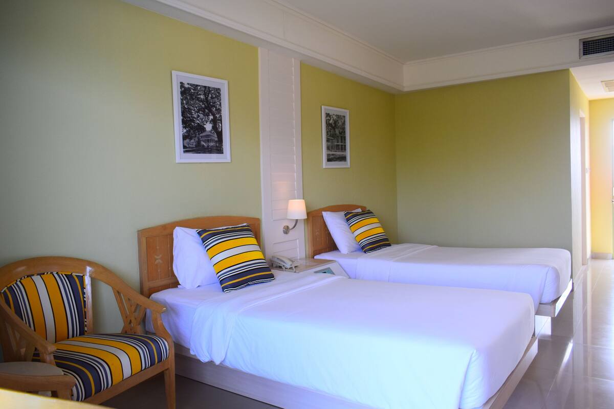 Ett hotellrum med två sängar, en trästol och två inramade tavlor på väggen.