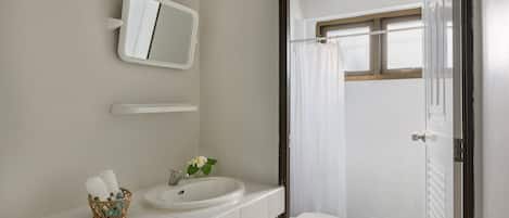 Un baño con un lavamanos blanco, un espejo, un inodoro y una cortina de ducha.