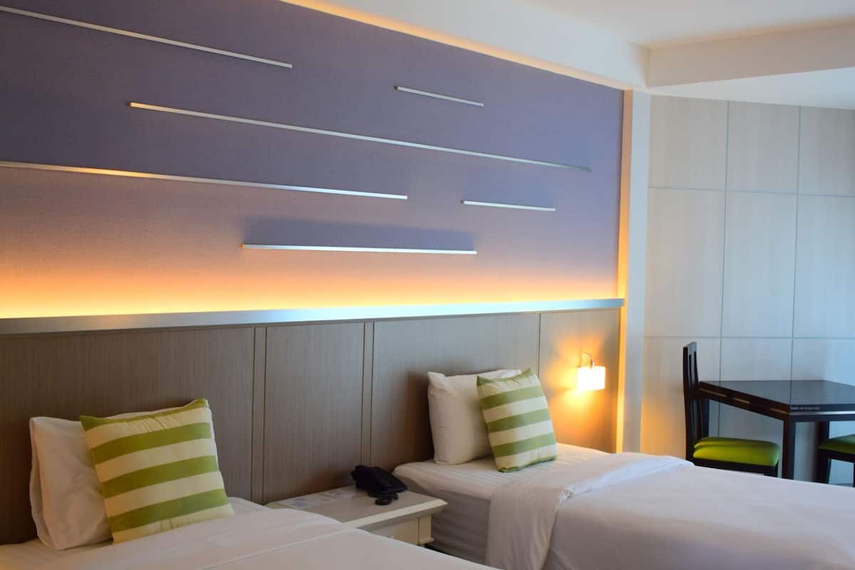 Ett hotellrum med två sängar, ett skrivbord, en stol och en väggmonterad lampa.
