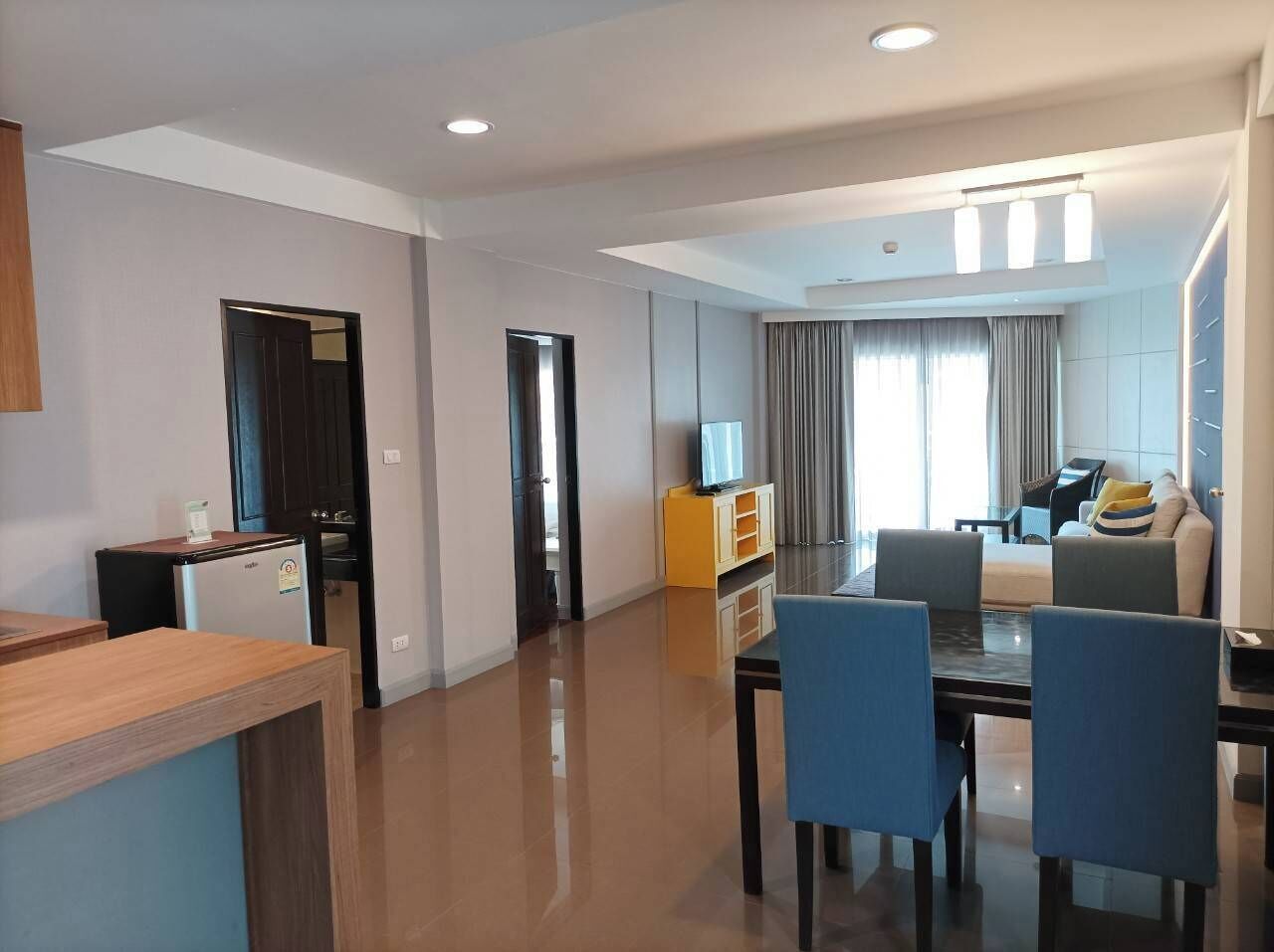 A modern hotel room with a dining area, a living room with a sofa and a piano, and a kitchen area.