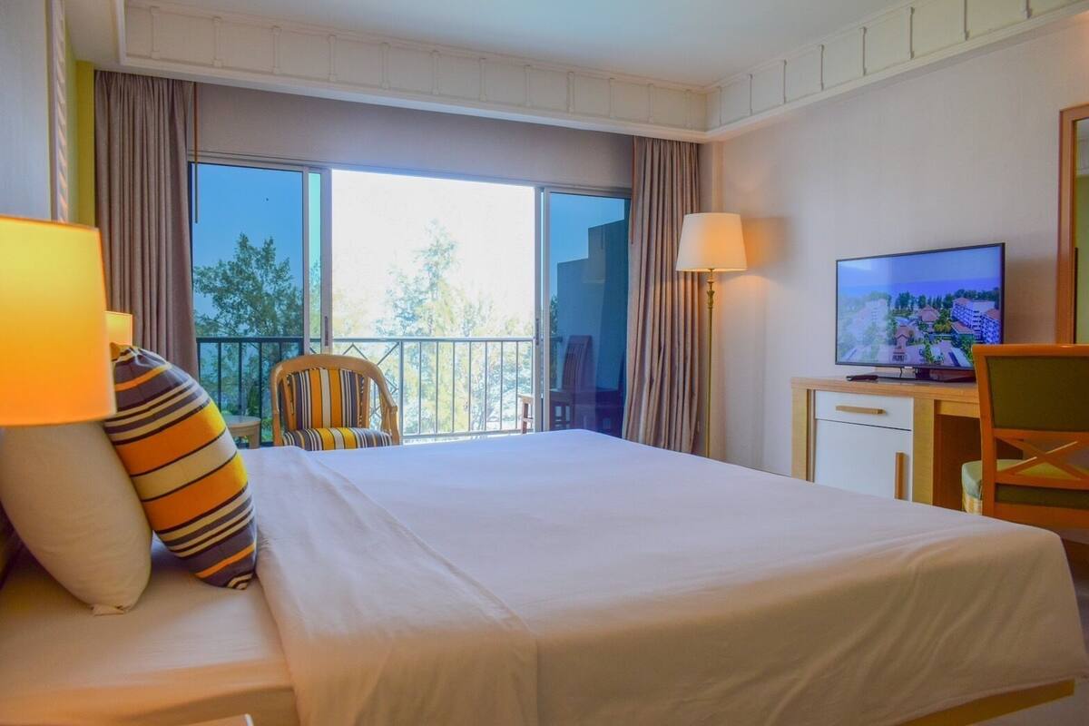Ett hotellrum med en stor säng, ett skrivbord, en tv och en balkong med gardiner.