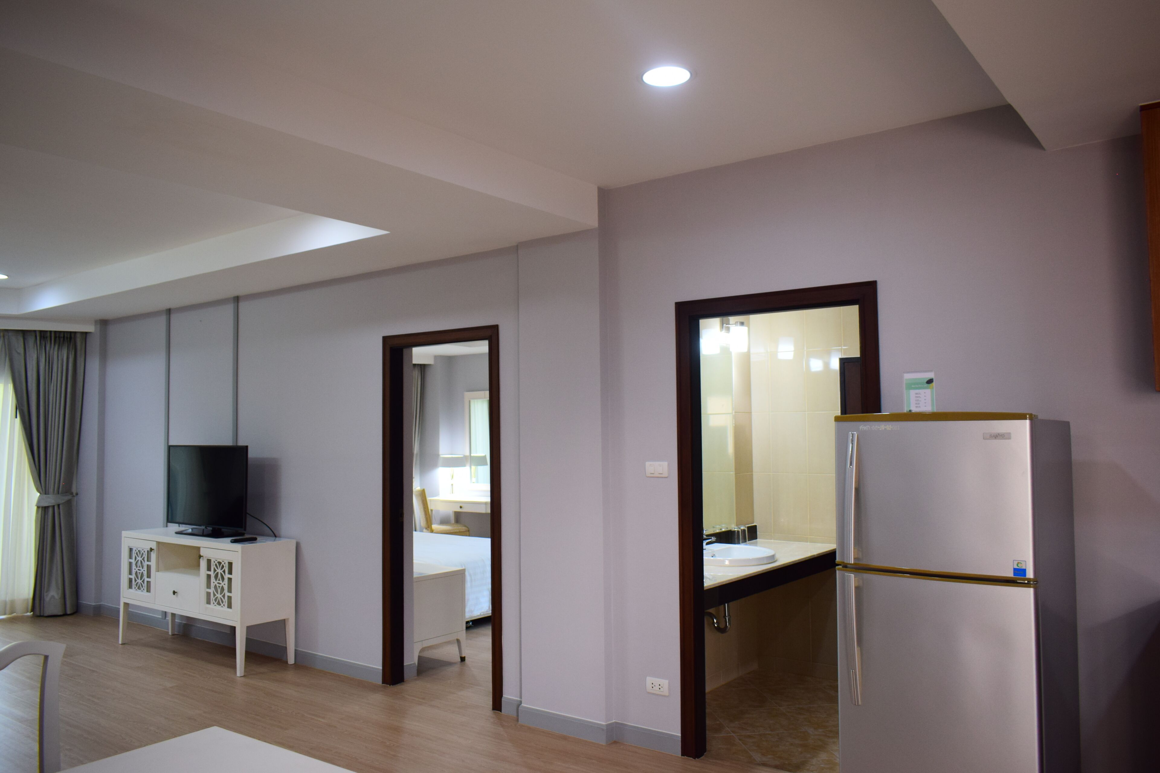A modern hotel room with a flat-screen TV, a white cabinet, a bed, and a refrigerator.