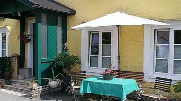 Ein Außenbereich mit Sitzgelegenheiten, Tisch, Stühlen, einem weißen Sonnenschirm und Topfpflanzen.