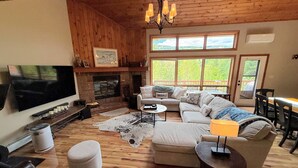 Una sala de estar acogedora con chimenea, televisor y un amplio ventanal con vistas a la vegetación.