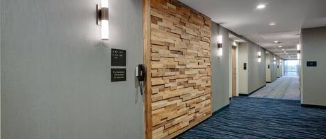 A hotel hallway with a wooden accent wall, a phone, and directional signs.