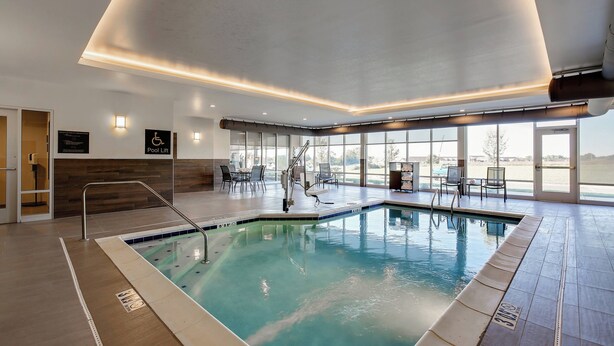 An indoor swimming pool with a pool lift, seating area, and large windows.