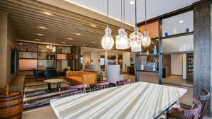 A modern hotel lobby with a large dining table, comfortable seating, and a wooden ceiling.