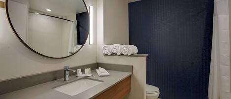 Un baño moderno con un espejo redondo, un lavabo, un inodoro y una cortina de ducha.