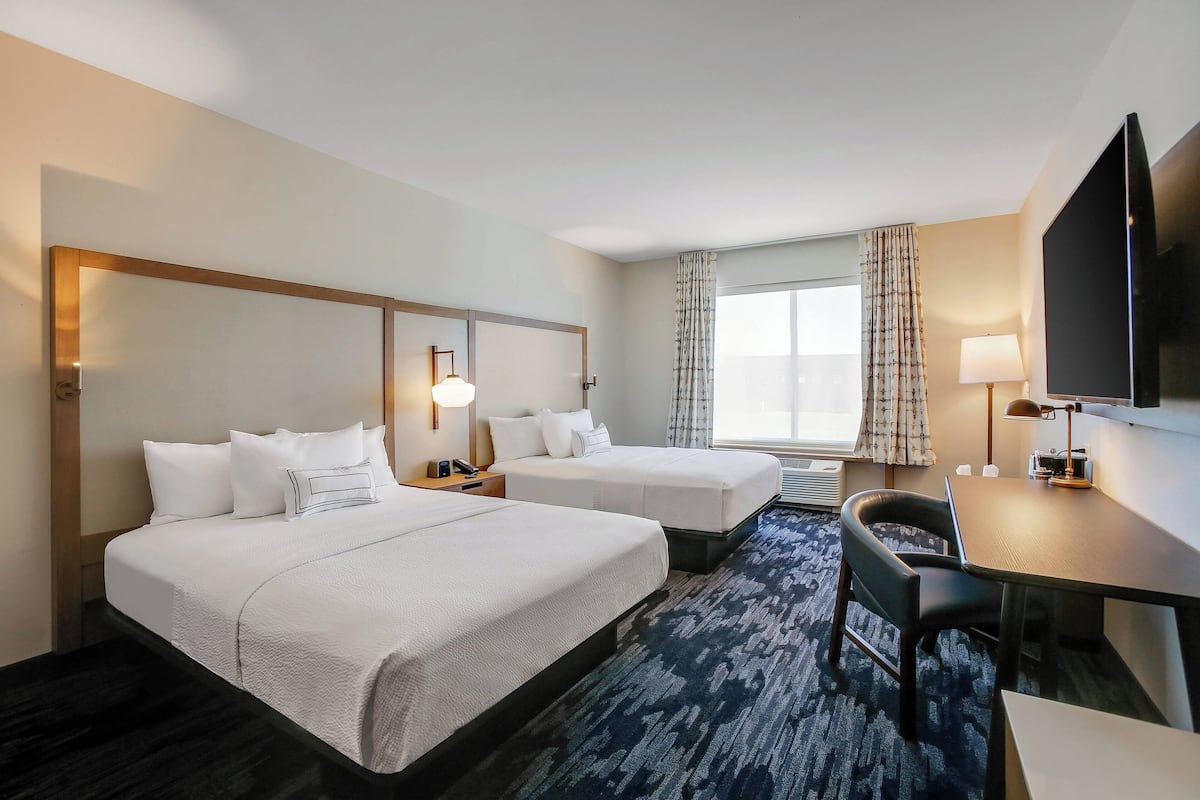 A hotel room with two beds, a desk, a chair, a TV, and a window with curtains.