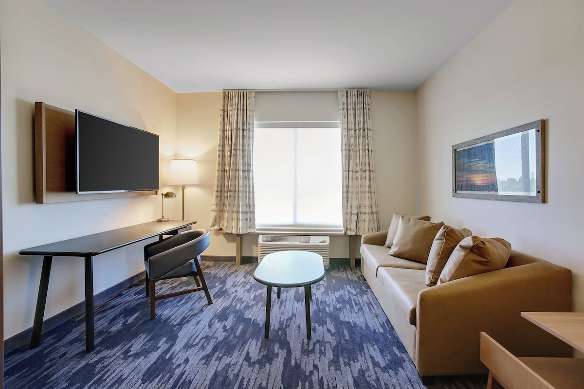 A hotel room with a flat-screen TV, a desk, a chair, a sofa, and a small table.