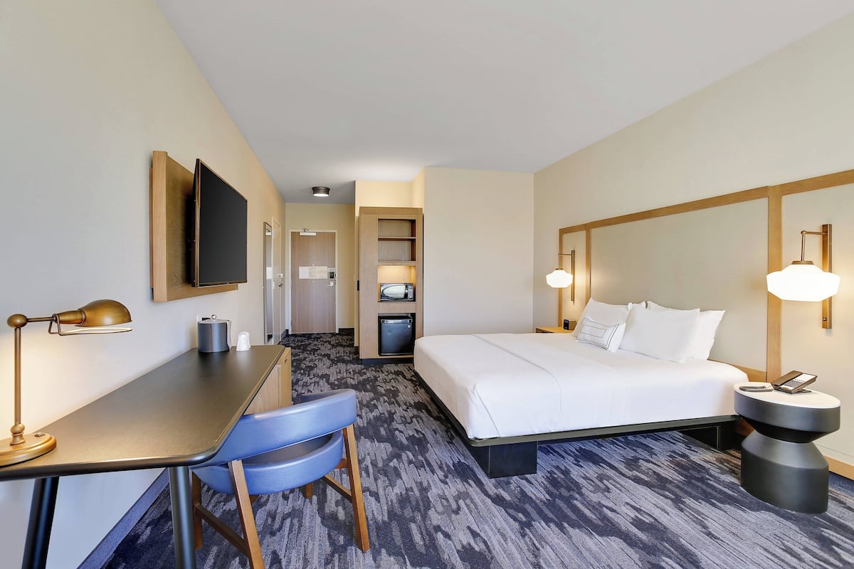 A hotel room with a bed, desk, chair, and a television.