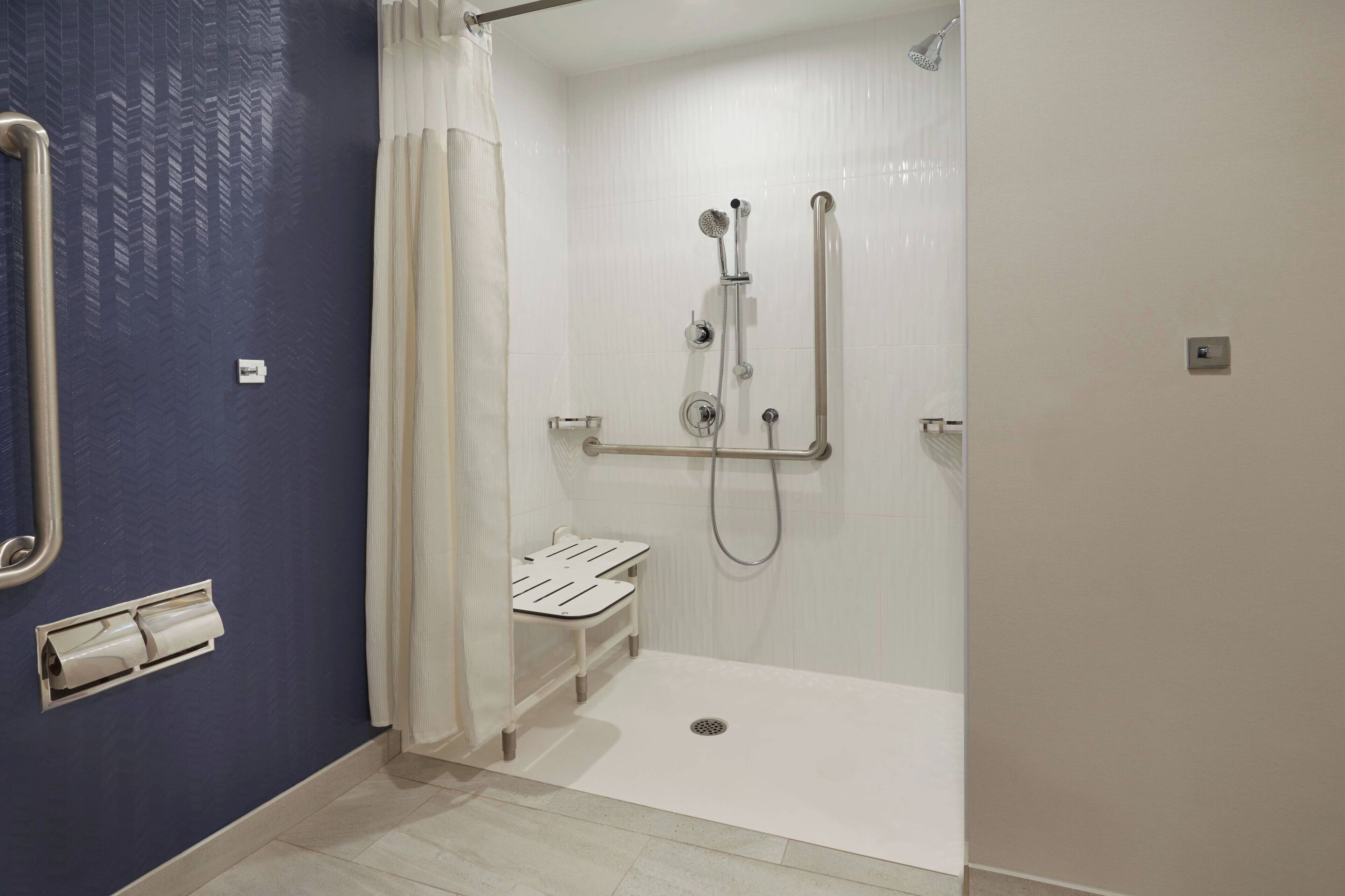 A bathroom with a shower, a toilet, and a handrail.