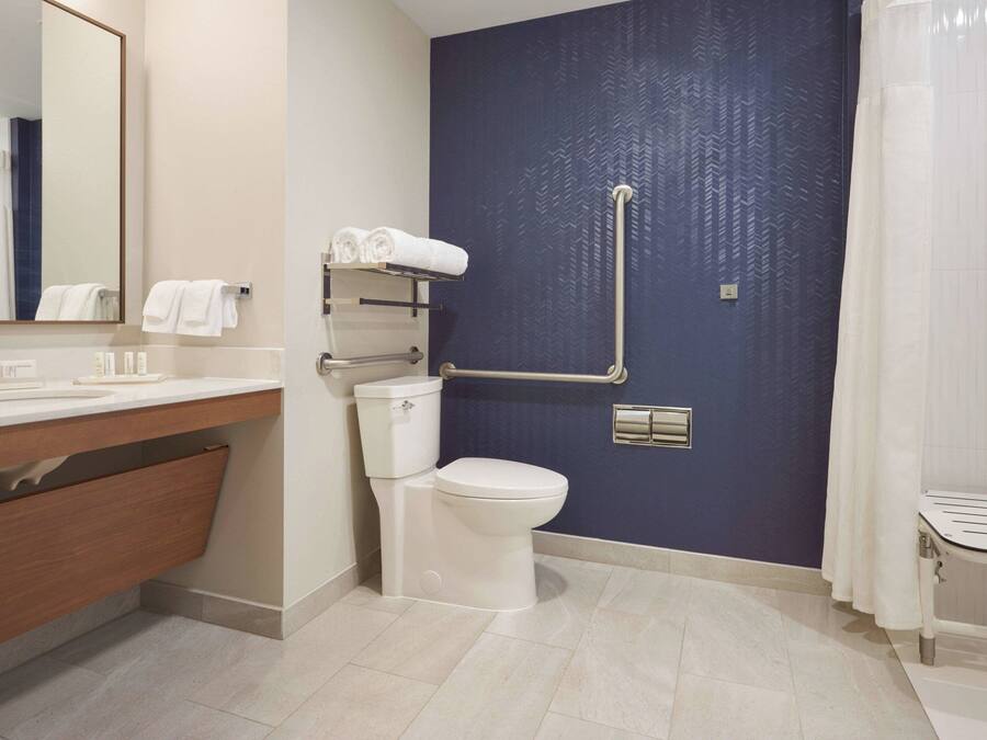 A modern bathroom with a white toilet, a sink with a mirror, a towel rack, and a shower area.