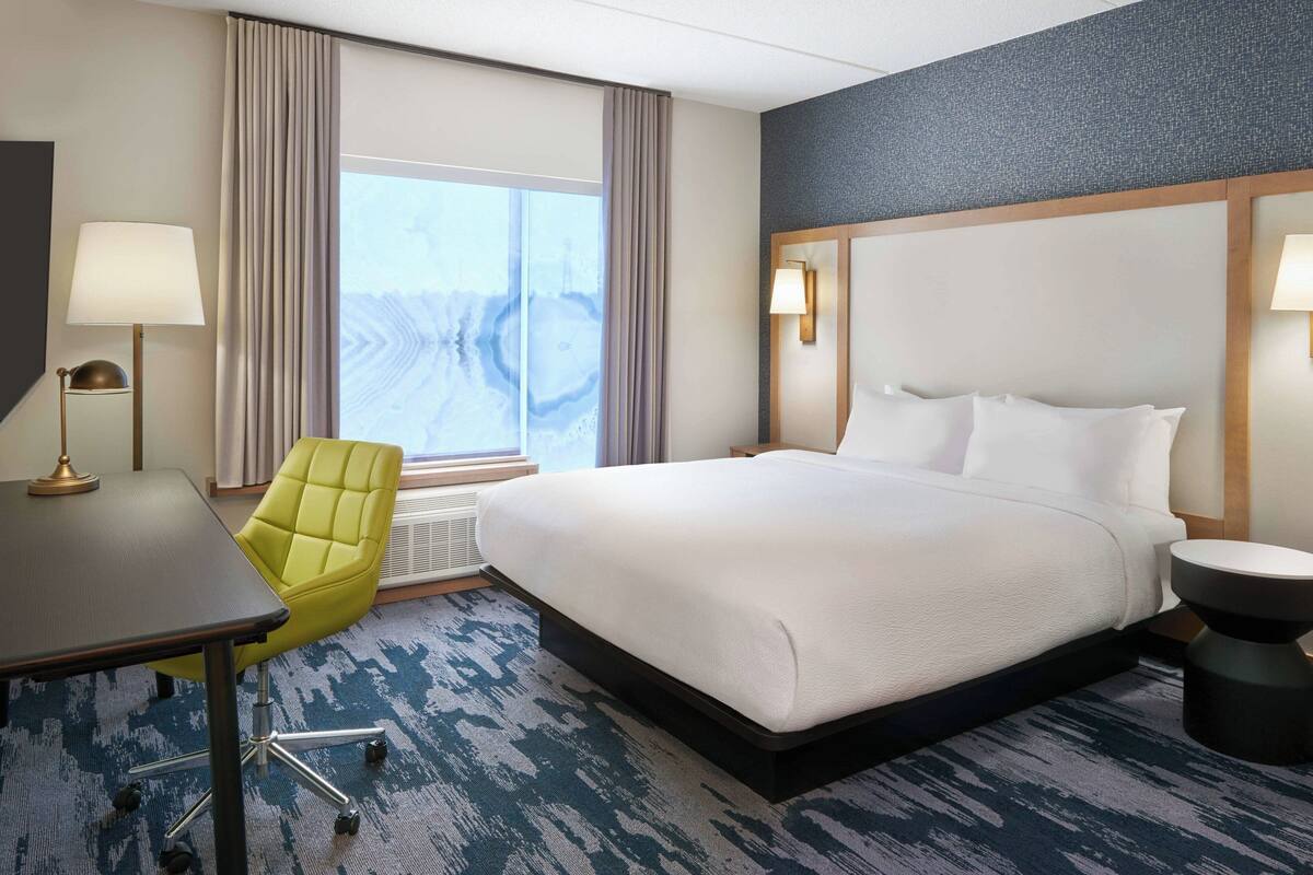 Une chambre d’hôtel avec un grand lit, un bureau, une chaise et une vue sur l’extérieur.