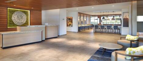 A modern reception area with a wooden ceiling, a reception desk, seating area with round tables and chairs, and a view of the outdoors through large windows.