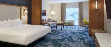 A hotel room with a large bed, a sofa, a small table, and a chair.