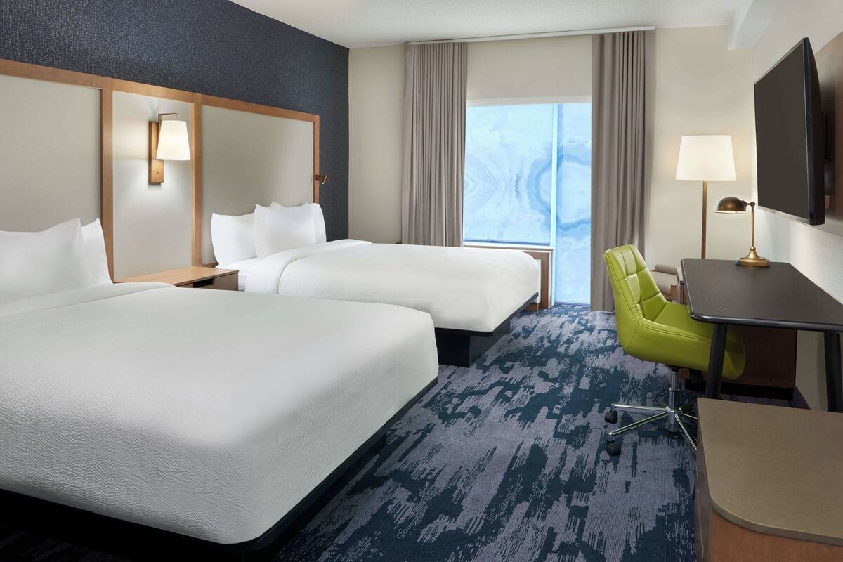 Une chambre d’hôtel avec deux lits, un bureau, une chaise, une télévision et une grande fenêtre.