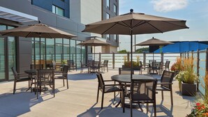 Een terras buiten met tafels, stoelen, parasols en potplanten.