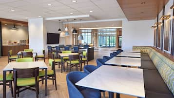 A modern dining area with multiple tables and chairs, a bar area, and large windows providing natural light.