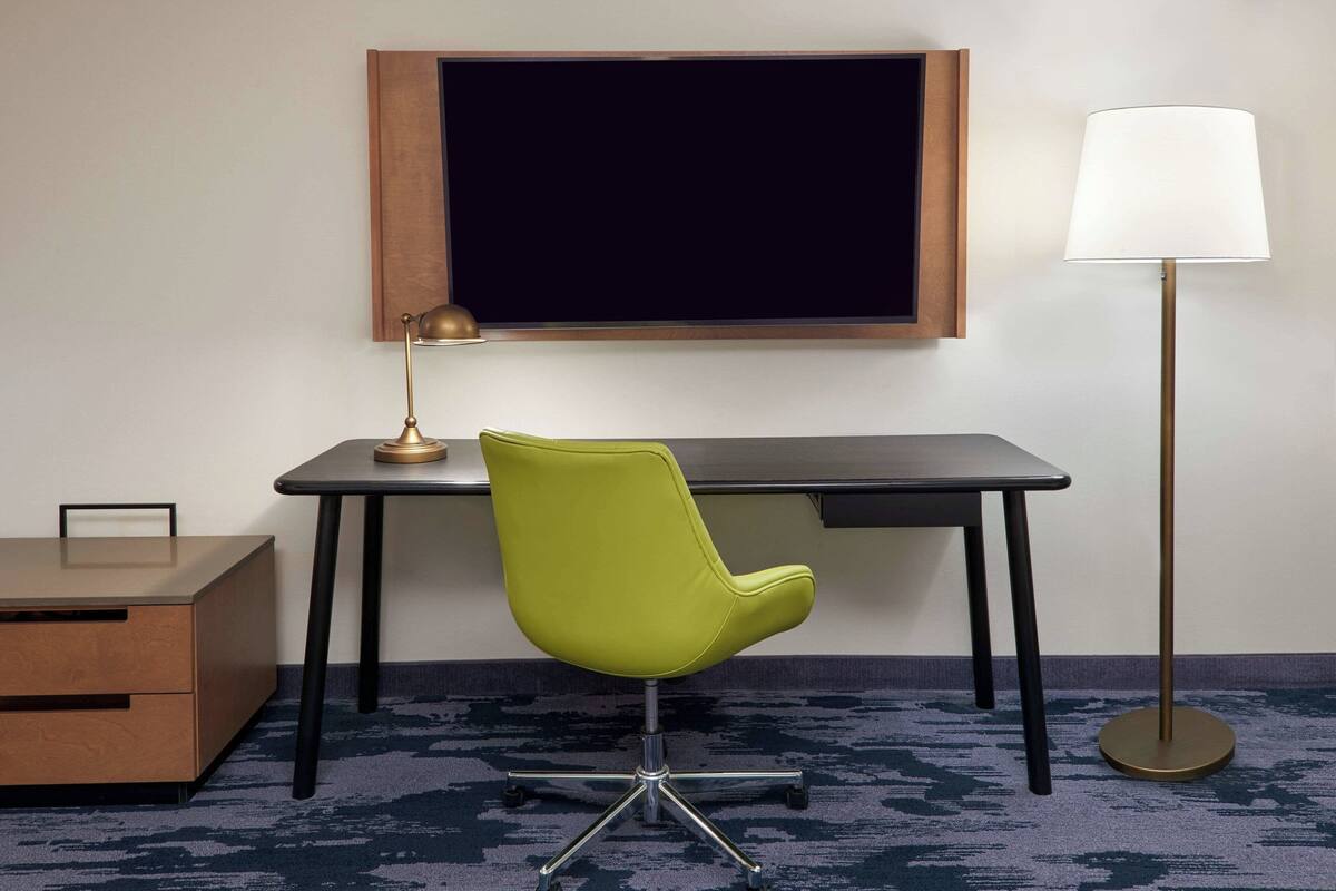 Une pièce comprenant un bureau, une chaise verte, une lampe et un meuble en bois.