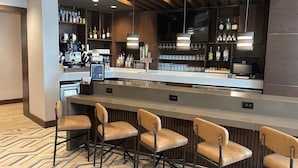 Un espace bar moderne doté d’un long comptoir, de nombreux tabourets et d’une variété de bouteilles et de verres disposés sur des étagères.
