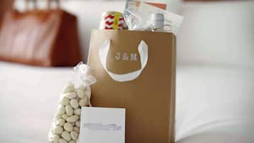 Una bolsa marrón de regalo J&M con asas, una tarjeta blanca y una bolsa de plástico con judías blancas sobre una cama.