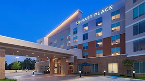 Un hôtel à plusieurs étages, reconnaissable à son grand panneau « HYATT PLACE », doté d’une entrée couverte et d’un espace piscine.