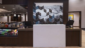 Un espace d’accueil au design moderne, comprenant un grand écran numérique, un comptoir d’accueil et un bar proposant une variété de boissons.