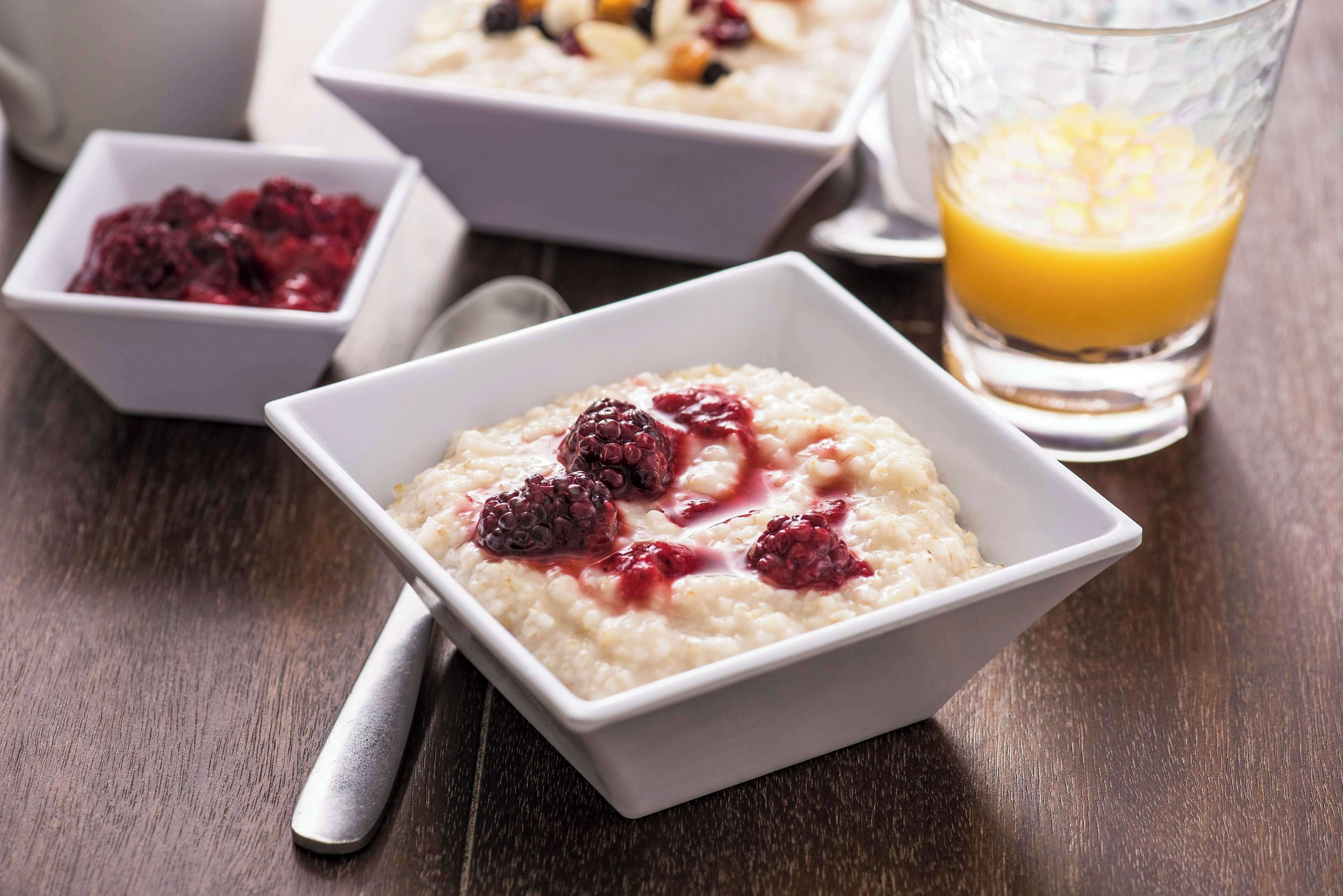 A bowl of oatmeal with berries and a glass of orange juice on a wooden table.
