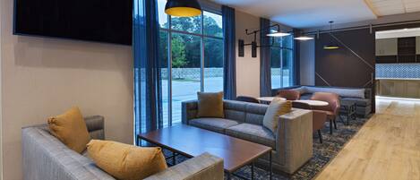 Eine moderne Hotelhalle mit einer Couch, Sesseln, einem Couchtisch und einem an der Wand montierten Fernseher.