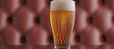 A tall glass of beer on a wooden table with a red leather background.