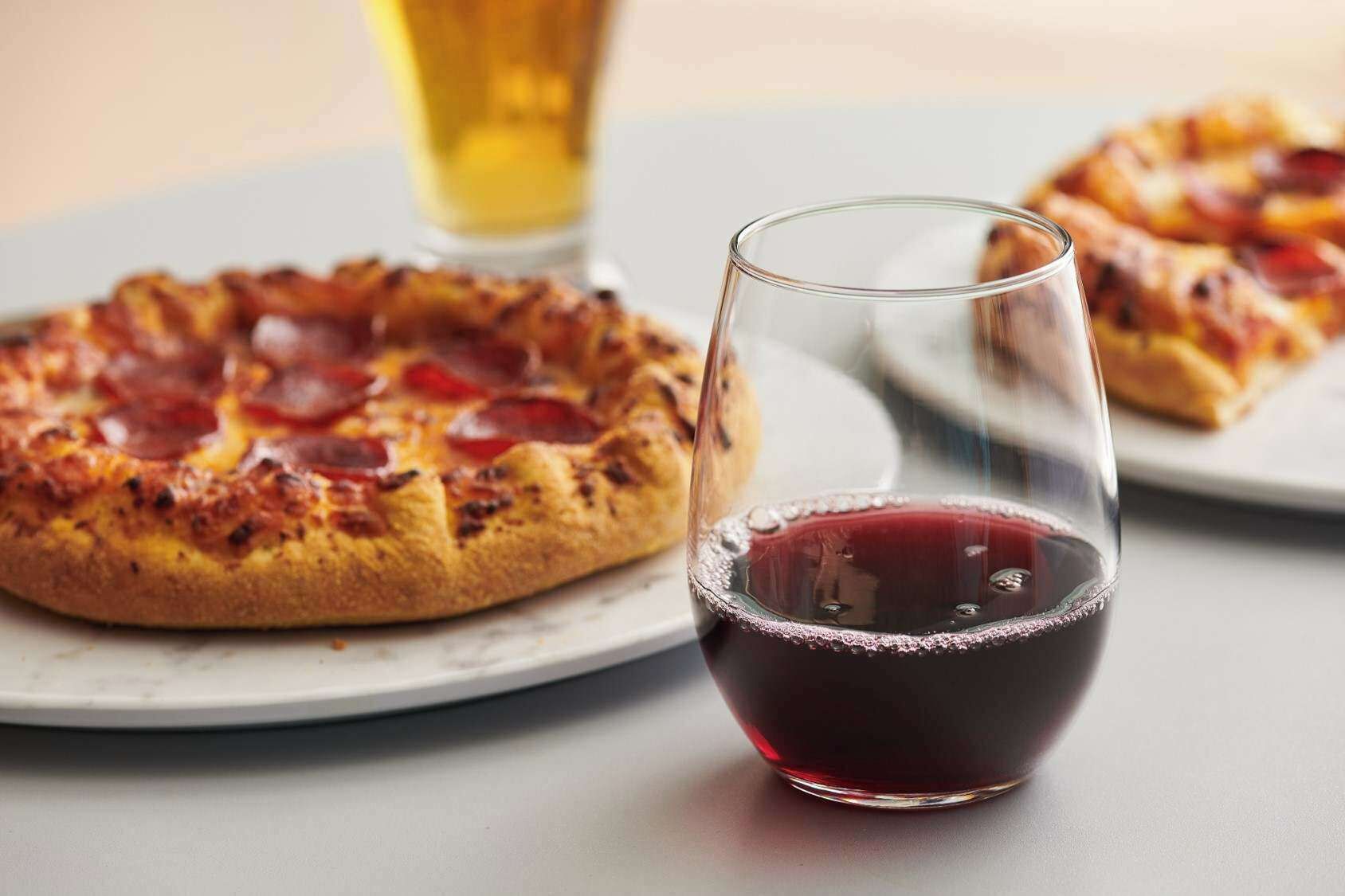 Una pizza en un plato con una copa de vino tinto.