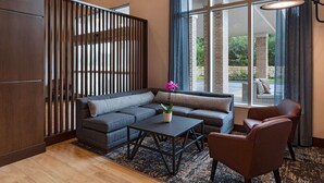 Un salon moderne avec un canapé d’angle, une table basse et un fauteuil. Une grande fenêtre offre une vue sur l’extérieur.