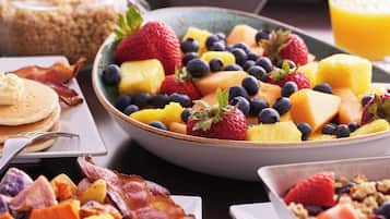A breakfast spread with pancakes, scrambled eggs, bacon, and various fruits like strawberries and blueberries.