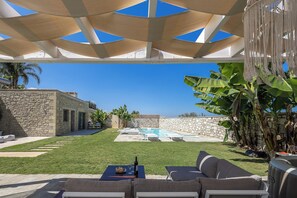 A backyard with a pool, outdoor furniture, and a stone wall.