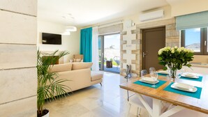 Una sala de estar moderna con un sofá, una mesa de comedor para dos personas y un ventanal con vistas.