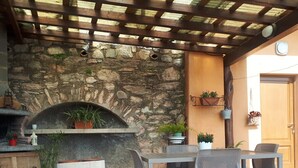 Une terrasse extérieure avec un mur en pierre, un four à pizza intégré et une pergola en bois.