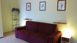 Un salon avec un canapé violet, une petite table de chevet blanche et trois tableaux encadrés accrochés au mur.