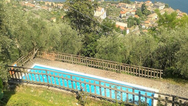 Une piscine entourée d’une clôture en bois, bordée de verdure et offrant une vue sur une ville côtière.