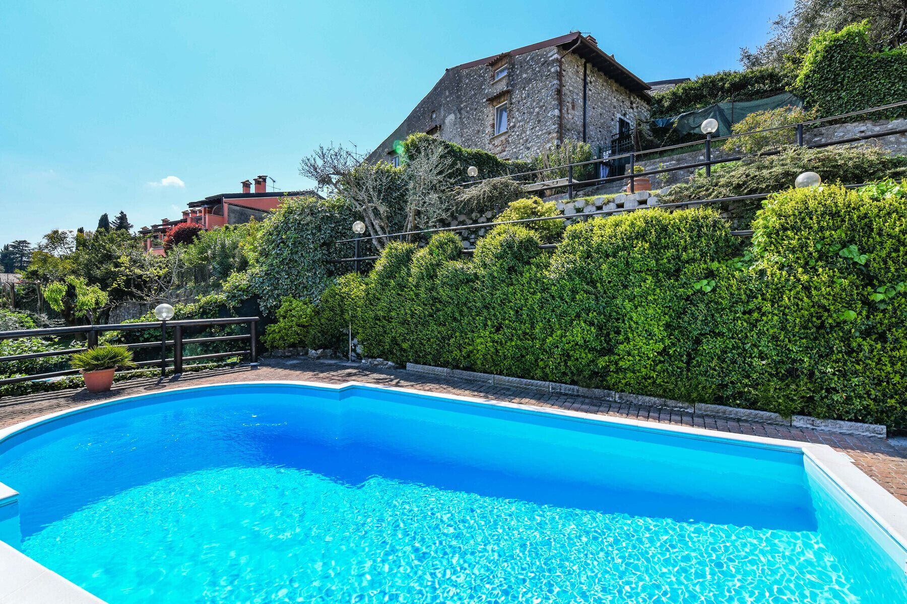 Une piscine à l’eau d’un bleu cristallin, entourée de haies bien entretenues et avec un bâtiment en pierre en arrière-plan.