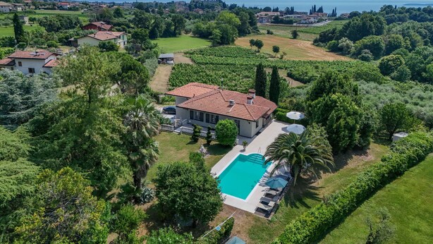 A villa with a swimming pool surrounded by lush greenery and a view of the sea. - villa Stefano in Moniga del Garda (Moniga del Garda)