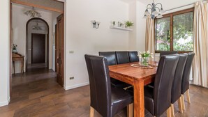 A dining area with a wooden table and black leather chairs, a chandelier, and a window with curtains. - villa Stefano in Moniga del Garda (Moniga del Garda)
