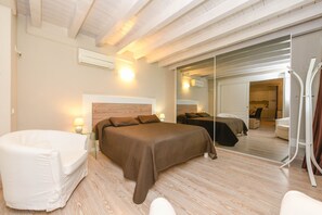 Un dormitorio moderno con una cama grande, un sillón blanco y un separador de vidrio.