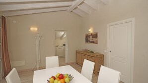 A dining area with a table set for four, a fruit bowl, white chairs, a wooden cabinet, and a white door. - Cà Rossa - Orchidea with stunning lake view (Toscolano-Maderno)